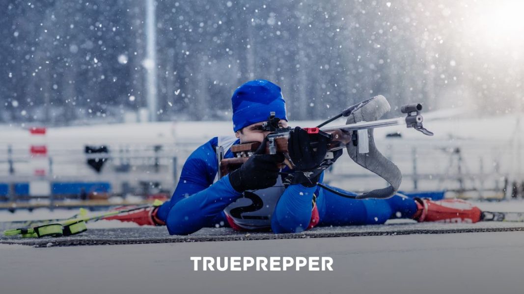 A biathlon skier laying prone in the snow aiming at a target.