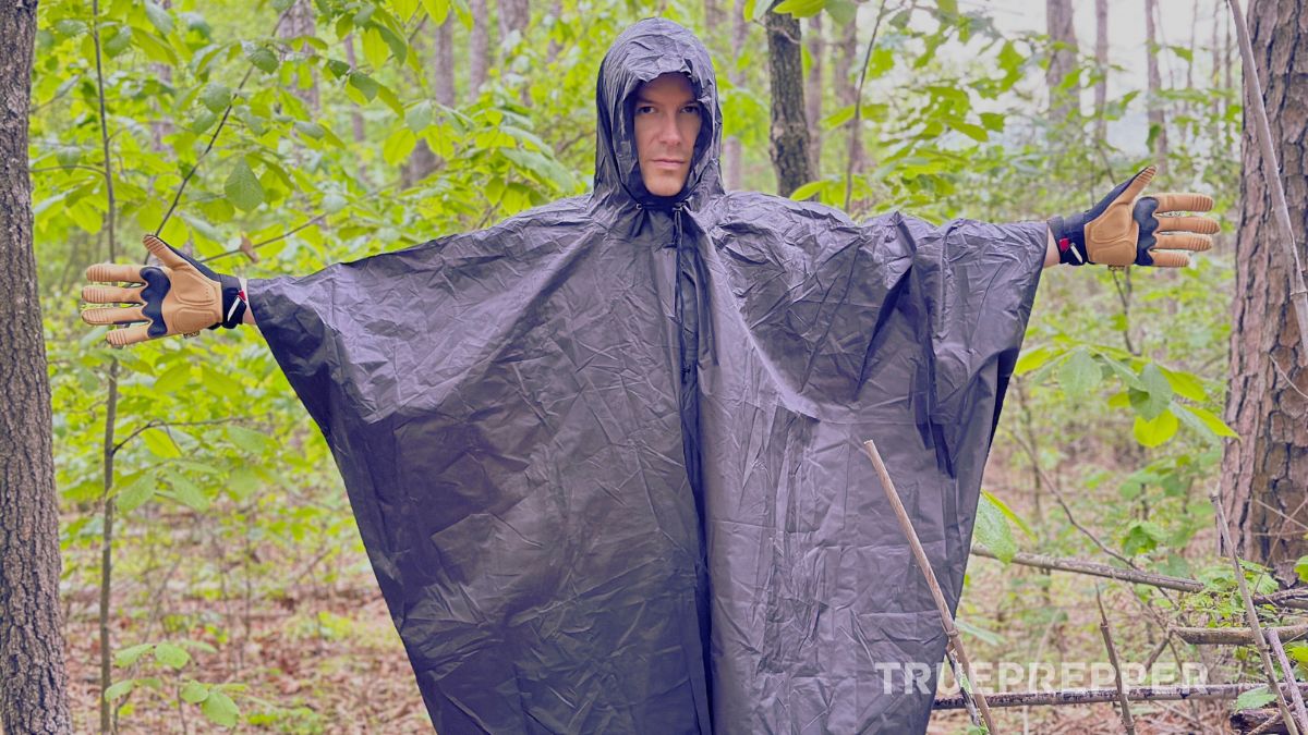 Sean standing in the rainy woods with his arms extended demonstrating the coverage of the Arcturus poncho.