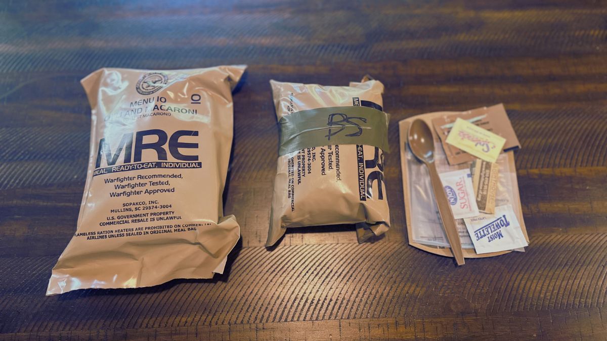 An unopened MRE and field stripped MRE with discarded contents on a wood table.