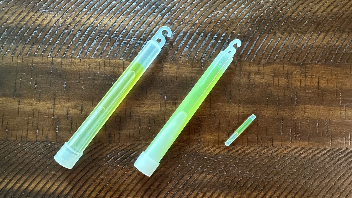 Six inch glowsticks for comparison to tiny survival kit glowstick on a wood table.
