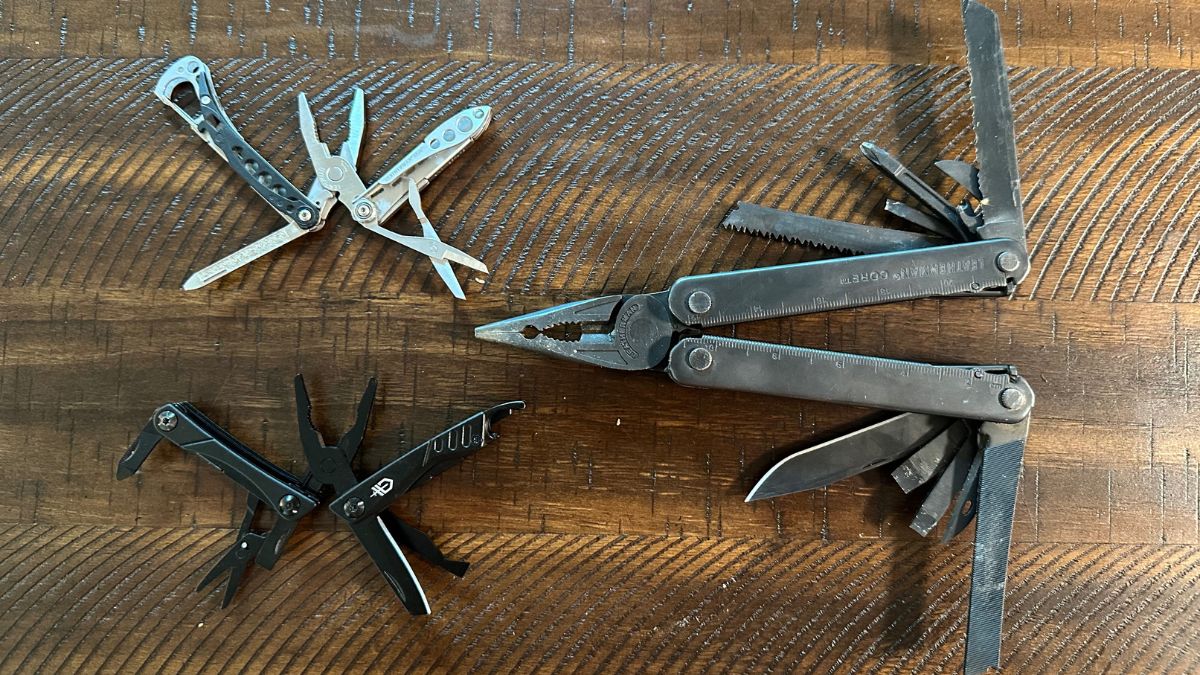 A full size multitool next to two EDC multitools showing the size difference on a wood table.