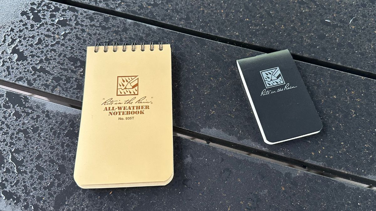 Rite in the Rain top-bound spiral notebook and small EDC notebook on a table in the rain.