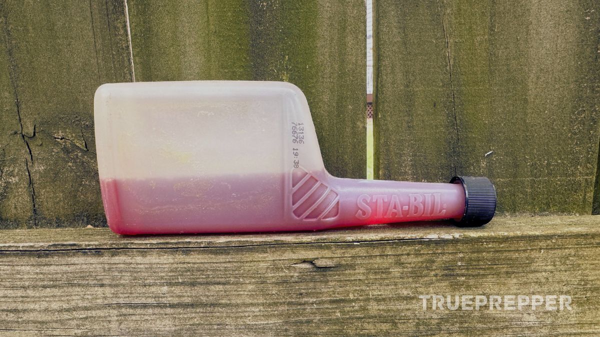 Half a bottle of red Sta-Bil laying on a fence.