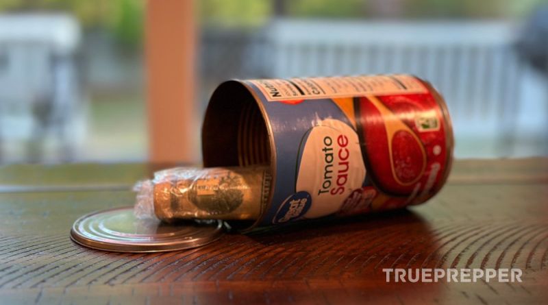 An empty tomato sauce can laying on a wood table with a bag of cash visible through it's resealable top.